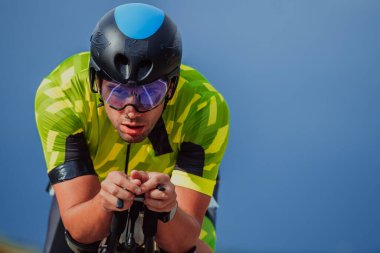 Full length portrait of an active triathlete in sportswear and with a protective helmet riding a bicycle. Selective focus.