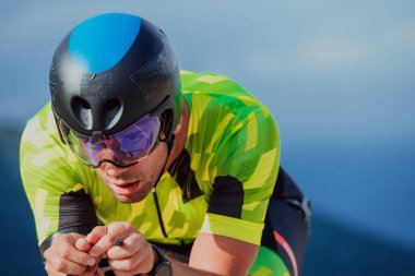 Close up photo of an active triathlete in sportswear and with a protective helmet riding a bicycle. Selective focus. 