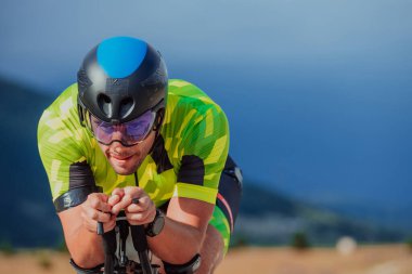 Close up photo of an active triathlete in sportswear and with a protective helmet riding a bicycle. Selective focus. 