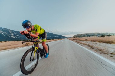 Full length portrait of an active triathlete in sportswear and with a protective helmet riding a bicycle. Selective focus.