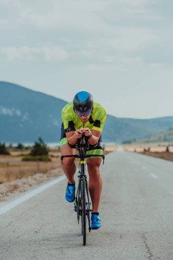 Full length portrait of an active triathlete in sportswear and with a protective helmet riding a bicycle. Selective focus.