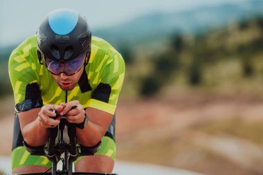 Close up photo of an active triathlete in sportswear and with a protective helmet riding a bicycle. Selective focus. 