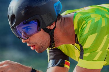 Close up photo of an active triathlete in sportswear and with a protective helmet riding a bicycle. Selective focus. 