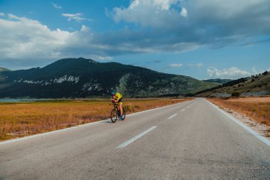 Full length portrait of an active triathlete in sportswear and with a protective helmet riding a bicycle. Selective focus.