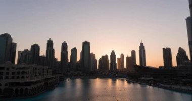 Dubai singing fountains at night view between skyscrapers. Timelapse of city skyline in dusk modern architecture and tall business and residental buildings in UAE capital. High quality 4k footage