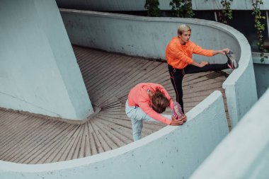 Two women warming up together and preparing for a morning run in an urban environment. Selective focus . 