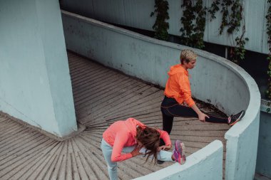 Two women warming up together and preparing for a morning run in an urban environment. Selective focus . 