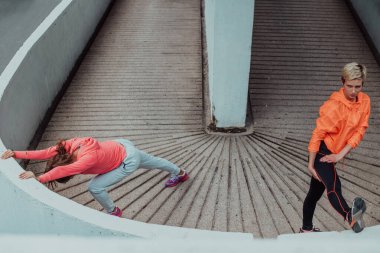 Two women warming up together and preparing for a morning run in an urban environment. Selective focus . 