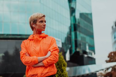 a woman in a sports outfit is resting in a city environment after a hard morning workout while using noiseless headphones. 