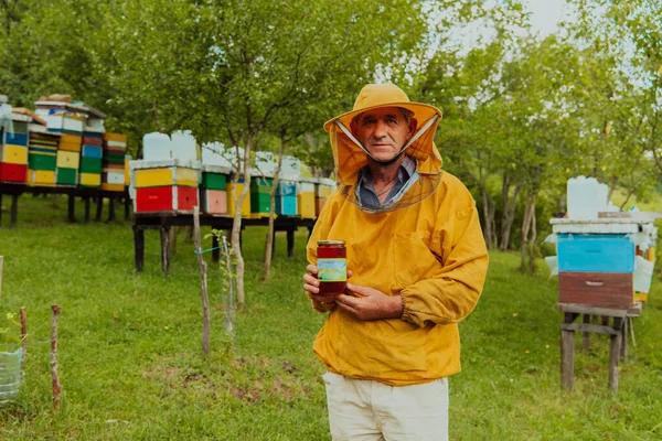 养蜂人站在草地上 手里拿着一罐蜂蜜 四周围着一盒蜂蜜和一个蜂蜜农场 — 图库照片
