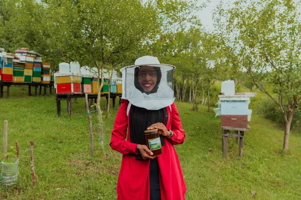Portrait of a Muslim African American woman in the beekeeping department of a honey farm holding a jar of honey in her hand.