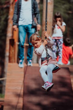 A little girl playing in the park. The concept of family socializing in the park. A girl swings on a swing, plays creative games. 