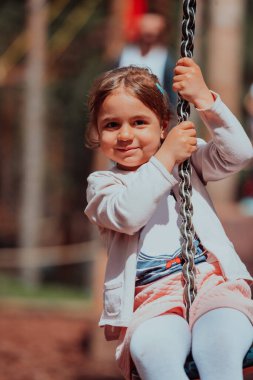 A little girl playing in the park. The concept of family socializing in the park. A girl swings on a swing, plays creative games. 