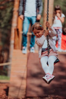 A little girl playing in the park. The concept of family socializing in the park. A girl swings on a swing, plays creative games. 