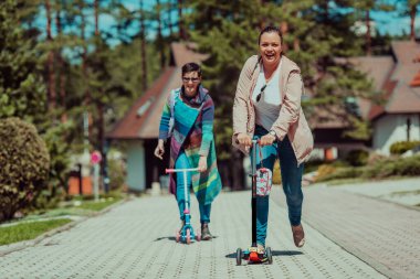 Two women having fun in the park while riding a scooter. 