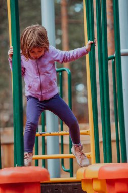 A little girl playing in the park. The concept of family socializing in the park. A girl swings on a swing, plays creative games. 