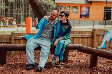 A romantic couple spends time in the park. A couple takes pictures on a beautiful sunny day while having a weekend off. 
