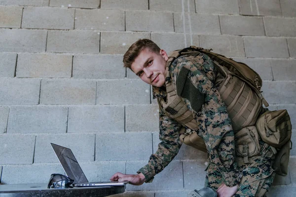 American soldier in military uniform using laptop computer for drone controlling and to stay in contact with friends and family.