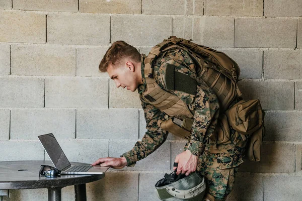 American soldier in military uniform using laptop computer for drone controlling and to stay in contact with friends and family.