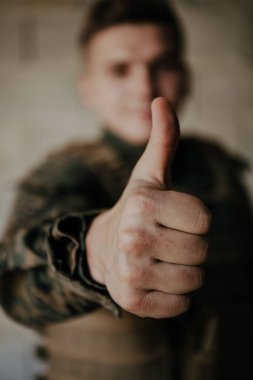 Asker eliyle bir başarı jesti yapar. Tam teçhizatlı bir asker taş bir duvarın önünde durur ve 