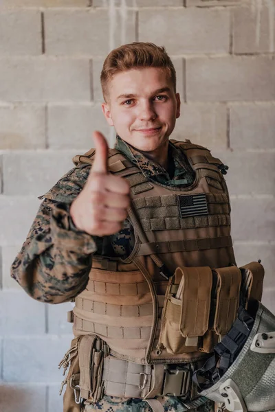 这个士兵用手做了一个成功的手势 一个身穿全套作战装备的士兵站在石墙前 用他的手指展示着这个标志 — 图库照片
