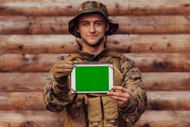 Asker, arkadaşları ve ailesiyle irtibatta kalmak için askeri kampta eski tahta duvarlara karşı tablet bilgisayar kullanıyor..