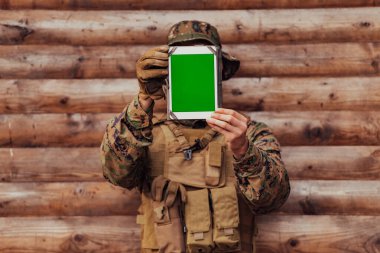 Asker, arkadaşları ve ailesiyle irtibatta kalmak için askeri kampta eski tahta duvarlara karşı tablet bilgisayar kullanıyor..