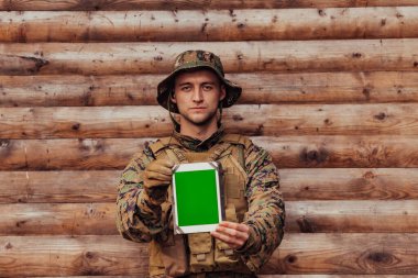 Asker, arkadaşları ve ailesiyle irtibatta kalmak için askeri kampta eski tahta duvarlara karşı tablet bilgisayar kullanıyor..