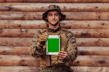 Asker, arkadaşları ve ailesiyle irtibatta kalmak için askeri kampta eski tahta duvarlara karşı tablet bilgisayar kullanıyor..