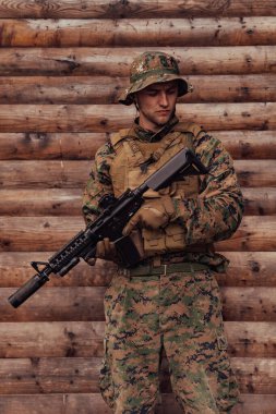 Elinde tüfekle üniformalı bir asker ahşap bir duvarın önünde duruyor. Bir asker orman üssünü düşmandan koruyor..