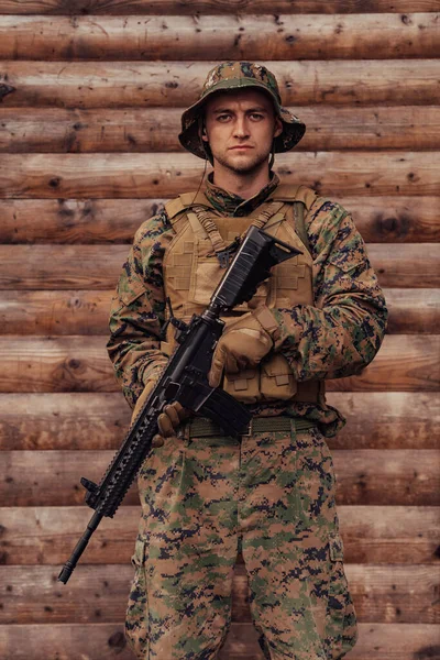 手にライフルを持った兵士が木の壁の前に立っている 兵士が敵から森の基地を守る — ストック写真
