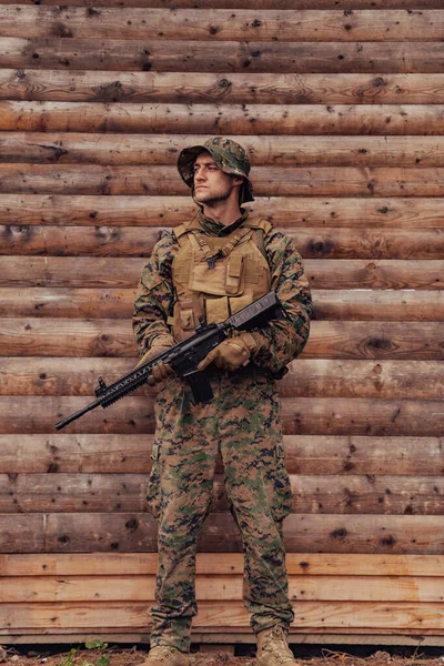 手にライフルを持った兵士が木の壁の前に立っている 兵士が敵から森の基地を守る — ストック写真
