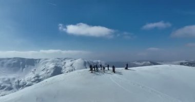 Bir dağın tepesinde kayakçıların ve snowboardcuların olduğu sinematik hava manzarası. Zirvede ya da üstte bir grup serbest gezici ya da taşra kayakçısıyla kış. Yörüngedeki çekim kalitesi yüksek.