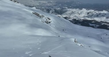 Bir dağın tepesinde kayakçıların ve snowboardcuların olduğu sinematik hava manzarası. Zirvede ya da üstte bir grup serbest gezici ya da taşra kayakçısıyla kış. Yörüngedeki çekim kalitesi yüksek.