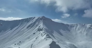 Havadan, yapraksız ağaçların üzerinden, karlı bir dağın üzerinden ve güzel karlı dağ zirvelerinin üzerinden. Kış ıssız, güneşli bir günde. Yüksek kalite 4k görüntü