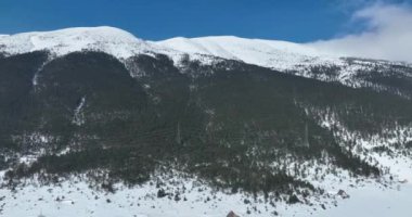 Havadan, yapraksız ağaçların üzerinden, karlı bir dağın üzerinden ve güzel karlı dağ zirvelerinin üzerinden. Kış ıssız, güneşli bir günde. Yüksek kalite 4k görüntü