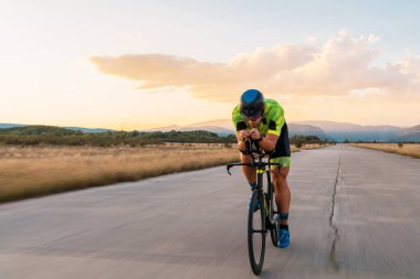  Gün batımında bisiklet süren bir triatloncu, maratona hazırlanıyor. Gökyüzünün sıcak renkleri kararlı ve odaklanmış çabaları için güzel bir zemin sağlar.