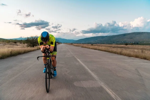 トライアスリートは日没時に自転車に乗り マラソンの準備をする 暖かい空の色は 彼の決定的かつ集中的な努力のための美しい背景を提供します — ストック写真
