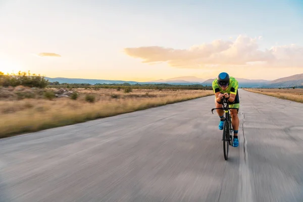Triathlete riding his bicycle during sunset, preparing for a marathon. The warm colors of the sky provide a beautiful backdrop for his determined and focused effort