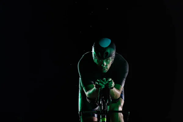一位三项全能运动员在漆黑的夜晚骑着他的自行车 努力为马拉松做准备 黑暗和他的自行车的灯光之间的反差产生了一种戏剧感 凸显了 — 图库照片