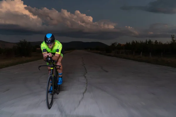 一位三项全能运动员在漆黑的夜晚骑着他的自行车 努力为马拉松做准备 黑暗和他的自行车的灯光之间的反差产生了一种戏剧感 凸显了 图库照片