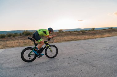  Gün batımında bisiklet süren bir triatloncu, maratona hazırlanıyor. Gökyüzünün sıcak renkleri kararlı ve odaklanmış çabaları için güzel bir zemin sağlar.