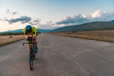  Gün batımında bisiklet süren bir triatloncu, maratona hazırlanıyor. Gökyüzünün sıcak renkleri kararlı ve odaklanmış çabaları için güzel bir zemin sağlar.