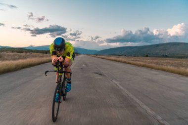  Gün batımında bisiklet süren bir triatloncu, maratona hazırlanıyor. Gökyüzünün sıcak renkleri kararlı ve odaklanmış çabaları için güzel bir zemin sağlar.