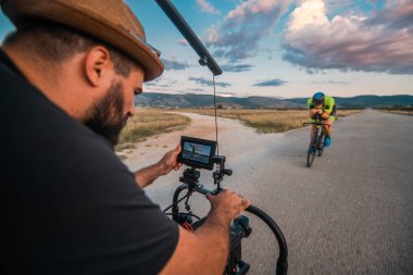 Bir triatloncunun yaklaşan maratona hazırlanması için bisiklet sürmesini kaydeden bir videograf.