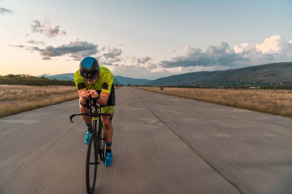 トライアスリートは日没時に自転車に乗り マラソンの準備をする 暖かい空の色は 彼の決定的かつ集中的な努力のための美しい背景を提供します — ストック写真