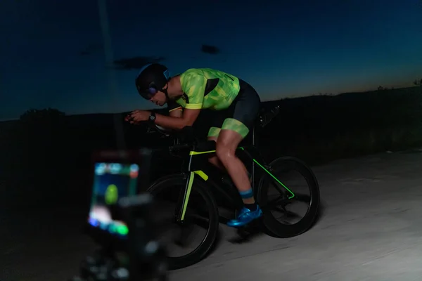将来のマラソンのために準備彼の自転車に乗ってトライアスリートを記録するビデオ撮影者 スポーツで成功するために必要な物理的な持久力と献身を可能にします — ストック写真