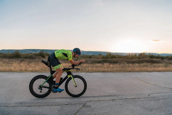 Triathlete riding his bicycle during sunset, preparing for a marathon. The warm colors of the sky provide a beautiful backdrop for his determined and focused effort