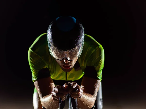 トライアスリートは夜の暗闇の中で自転車に乗り マラソンの準備をするために自分自身を押します 暗闇と彼の自転車の光のコントラストは ドラマの感覚を作成し 強調表示されます — ストック写真