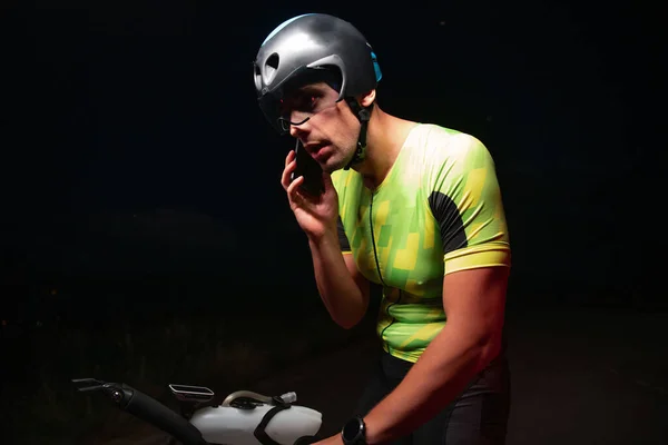 一位三人组运动员在从一个严酷的夜间自行车训练中休息时使用智能手机 高质量的照片 — 图库照片